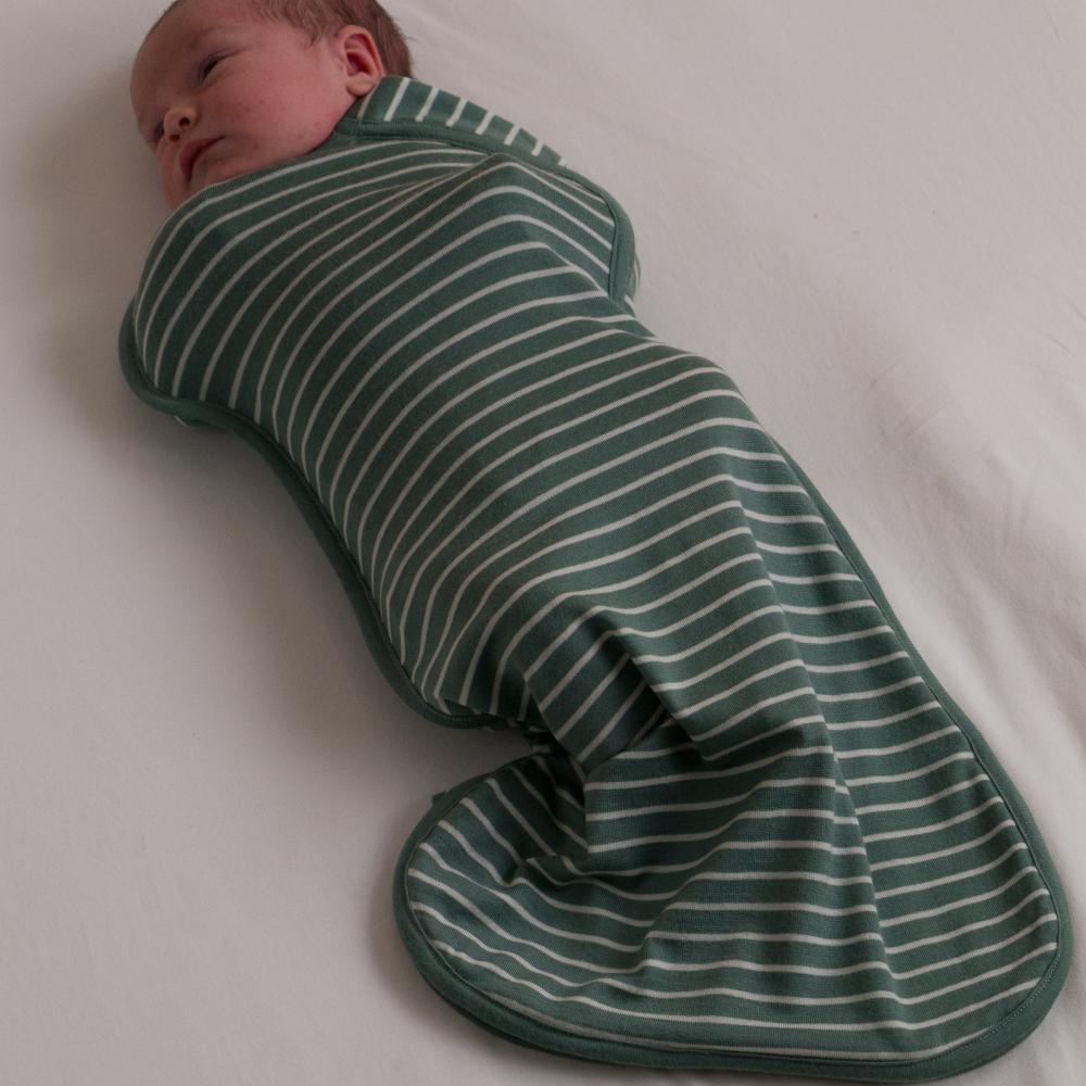 Baby swaddled in a green and white striped swaddle on a light background