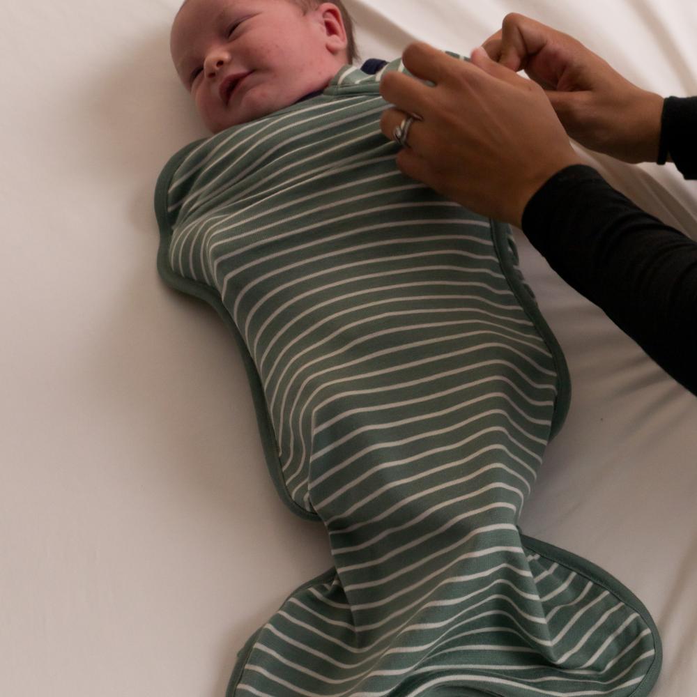 Baby wrapped in a green and white striped merino swaddle on a white surface