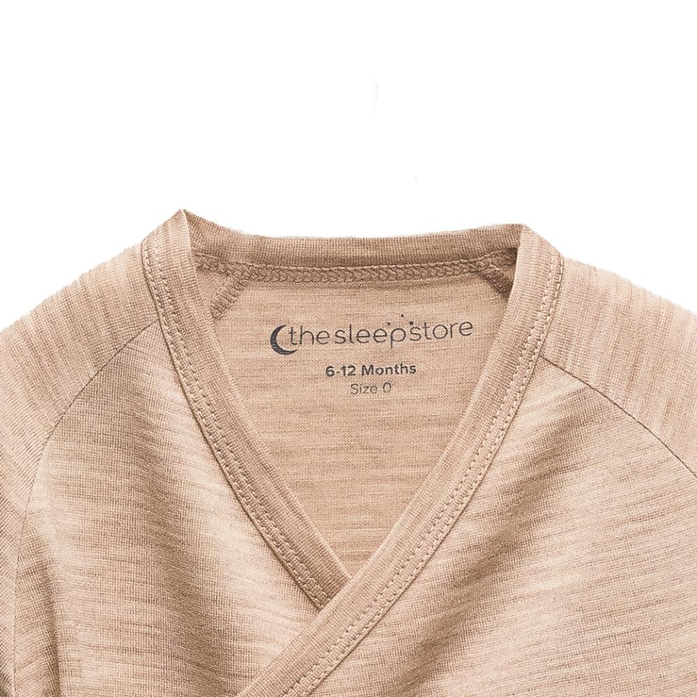 Close-up of a baby wrap-style shirt in a heathered light tan color, showing the inner neck label with the brand 'the sleepstore'.
