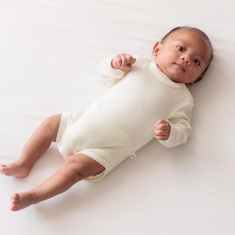 Baby lying on a white surface wearing a white bodysuit.