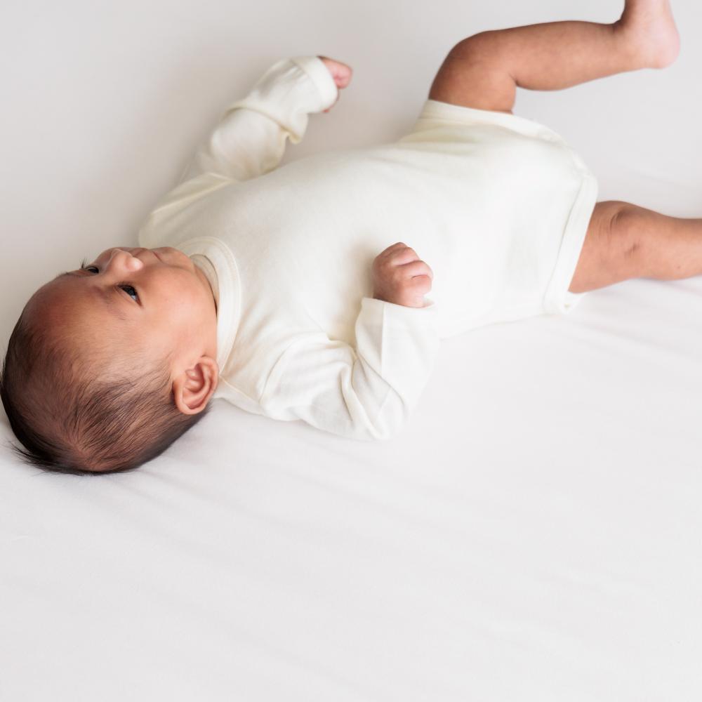 Baby lying on a white surface wearing a white bodysuit.