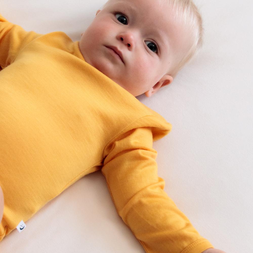 Young baby wearing a yellow long sleeve jersey merino bodysuit