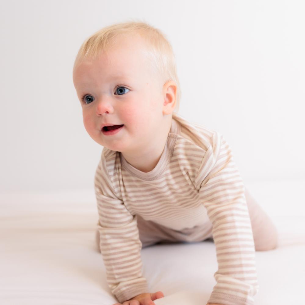 Baby in a striped outfit sitting on a white surface