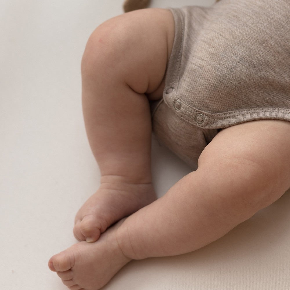 Close-up of a baby's legs and feet wearing a beige onesie on a light background