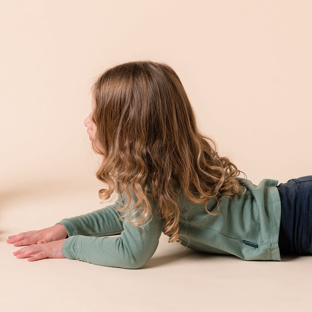 Young child wearing merino long sleeve top while laying on stomach