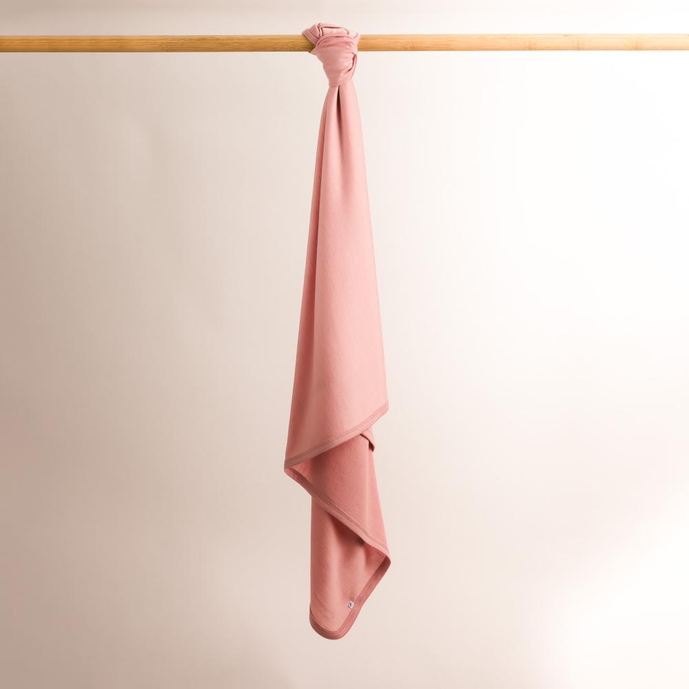 Pink merino baby blanket hanging on a wooden rod against a beige background