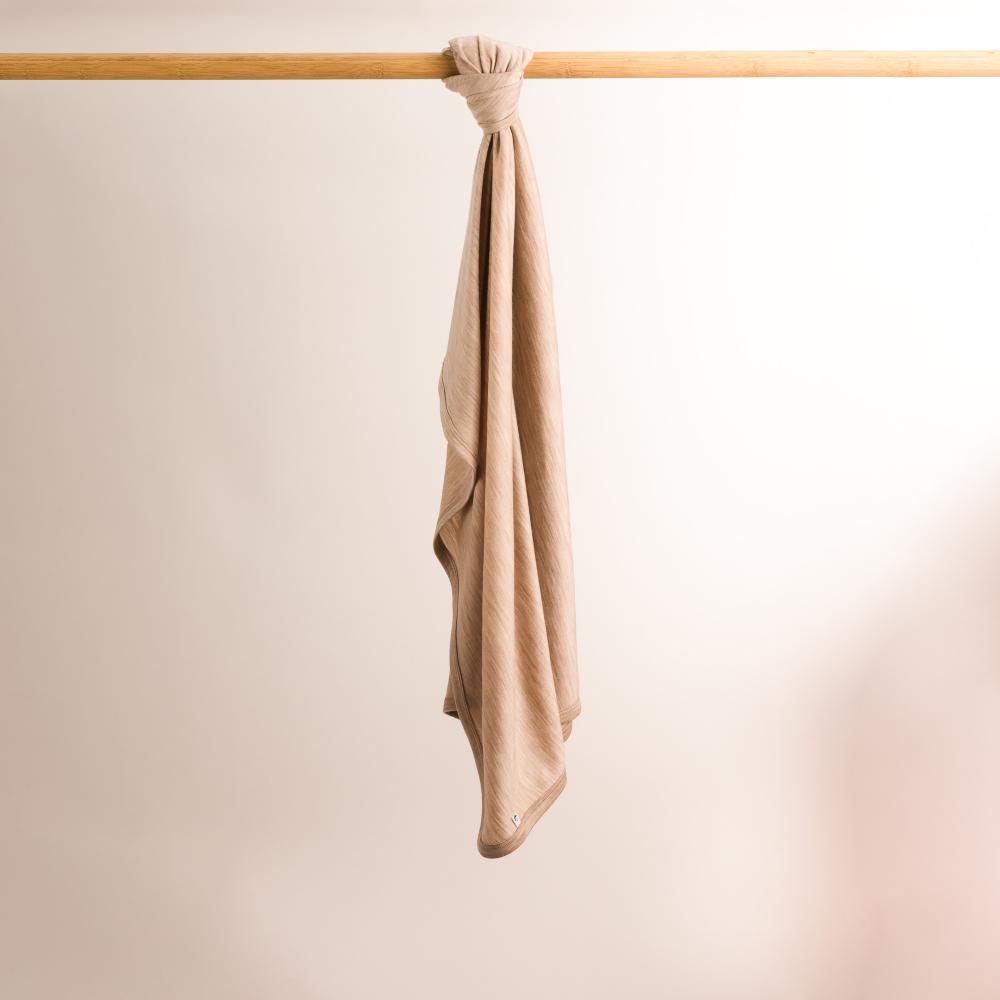 Beige merino baby blanket hanging on a wooden rod against a plain background