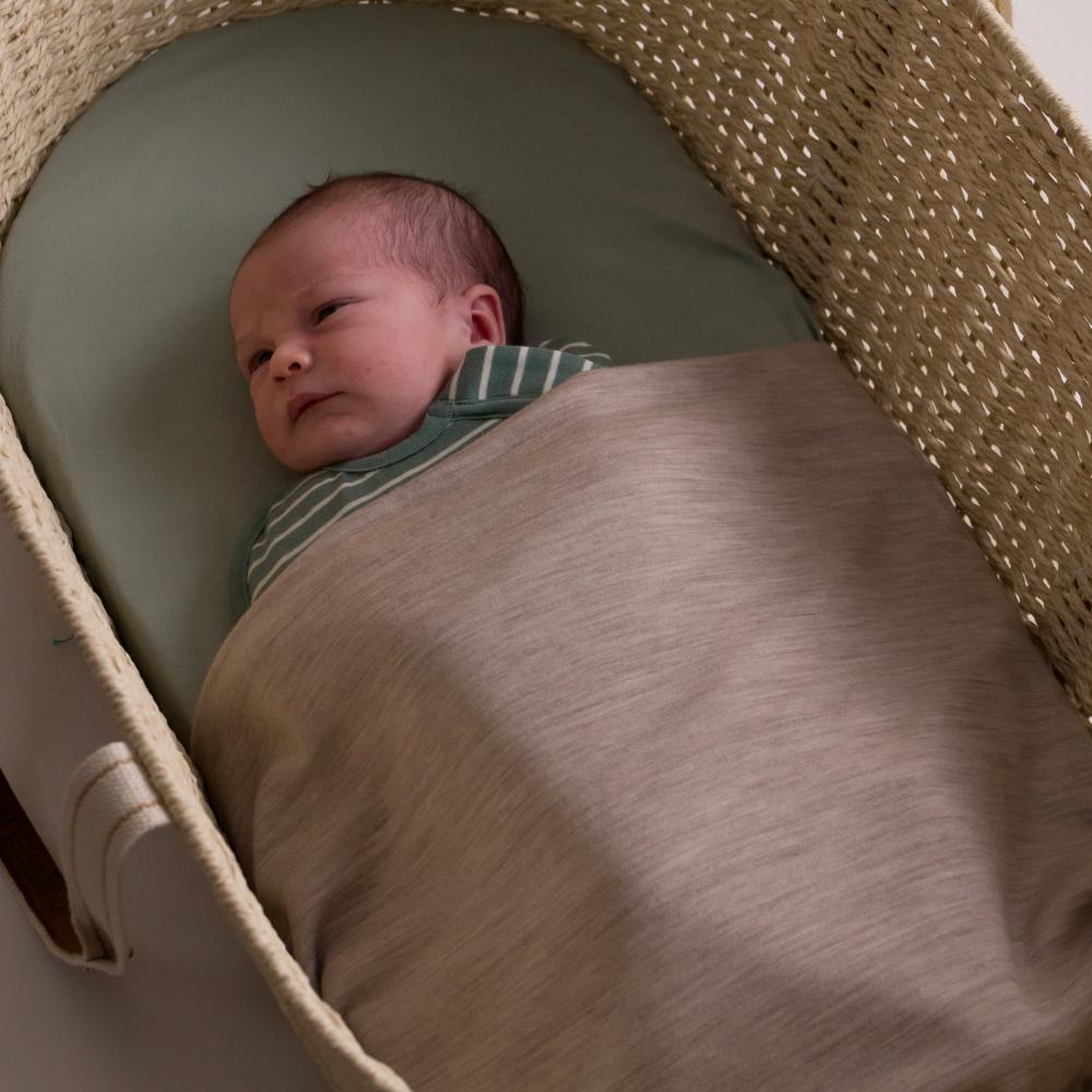 Baby wrapped in merino blanket laying moses basket