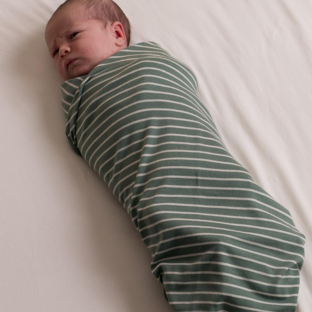 Newborn baby wrapped in a green and white striped merino swaddle on a white background