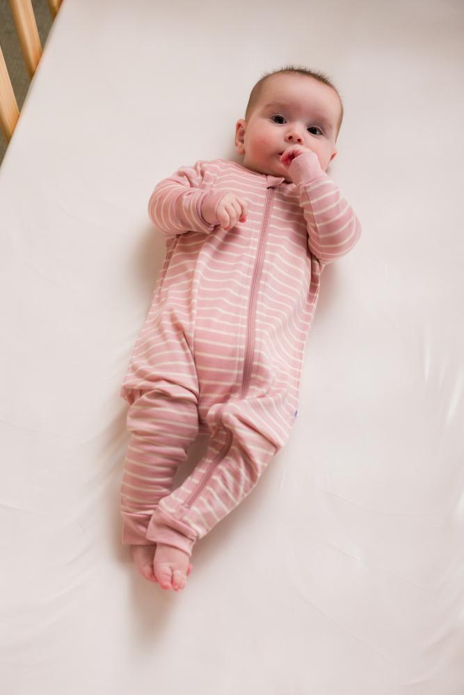 Baby in a pink striped merino zipsuit lying on a white surface