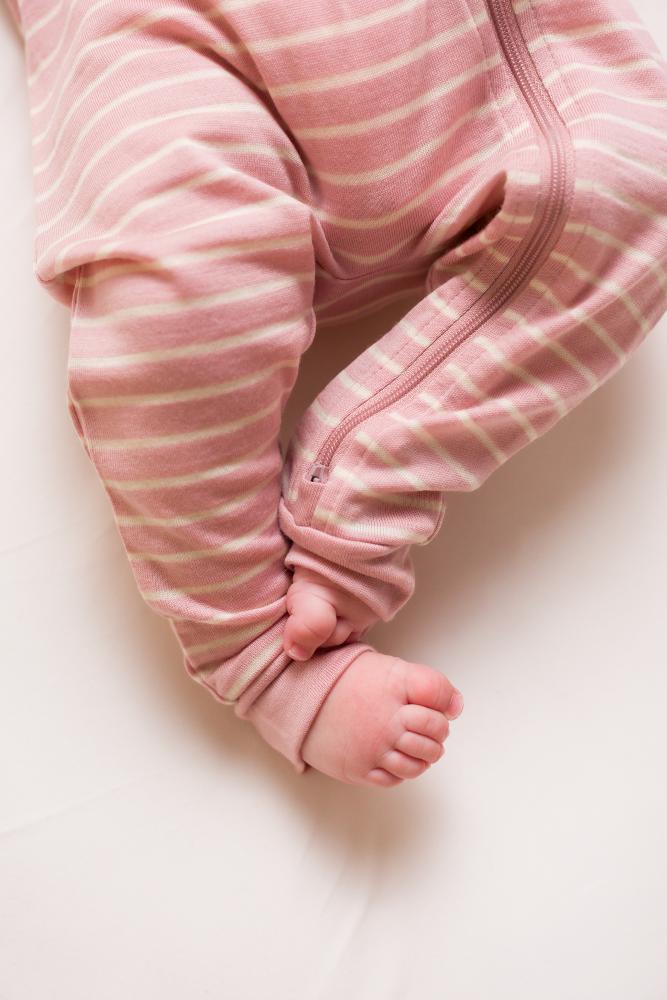 Close-up of a baby's legs in pink striped merino pajamas on a light background