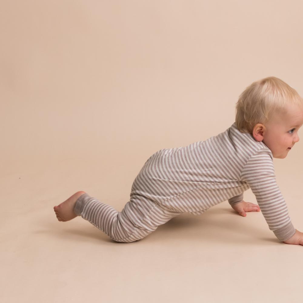 Baby in a striped merino onesie crawling on a beige surface by the sleep store