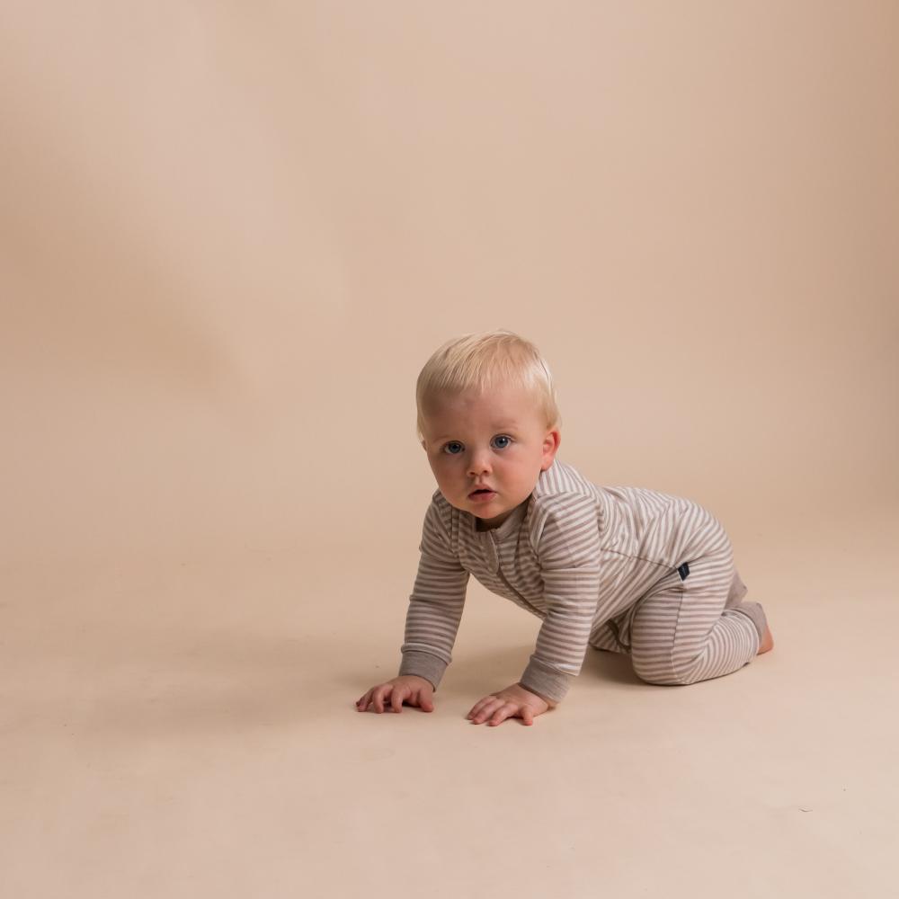Baby in a striped merino onesie crawling on a beige background