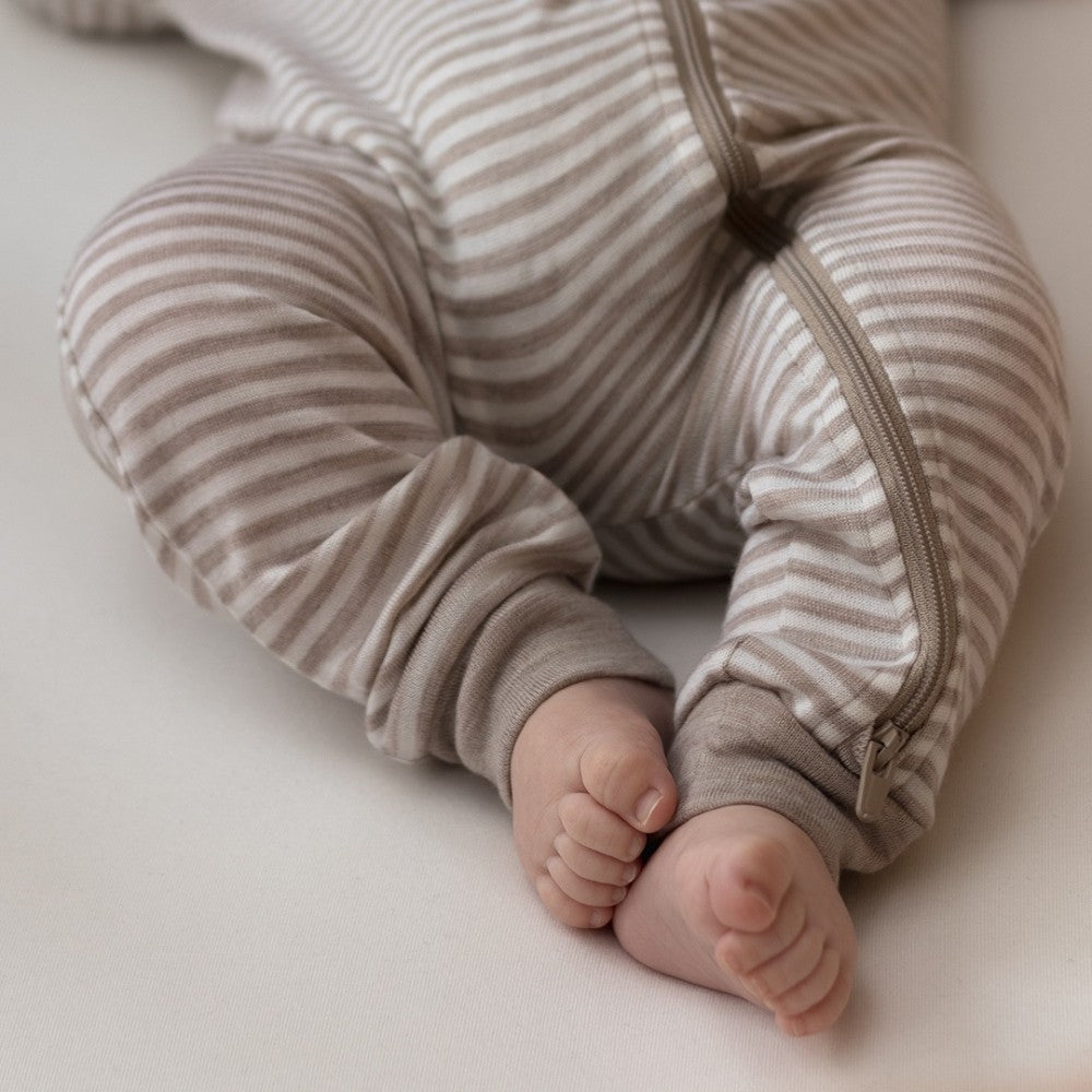 Close-up of a baby's legs in striped merino pajamas on a light background