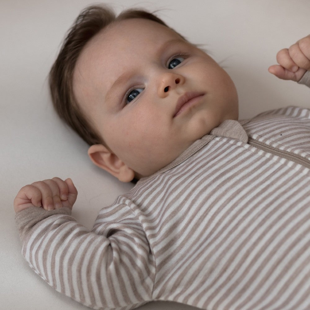 Baby wearing a merino striped onesie lying on a white surface by the sleep store