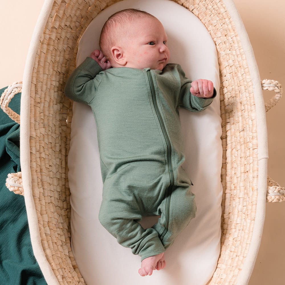 Newborn baby in a merino onesie lying in a woven crib with a beige background