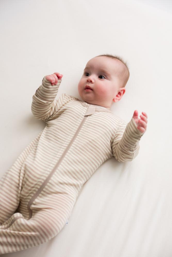 Baby lying on a white surface wearing a beige merino onesie with zipper.