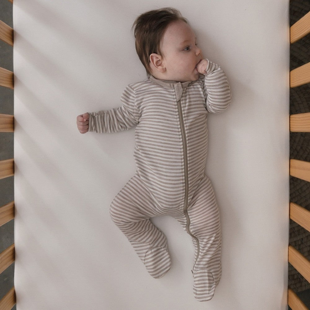 Baby in a striped merino onesie lying on a crib with a wooden frame by the sleep store