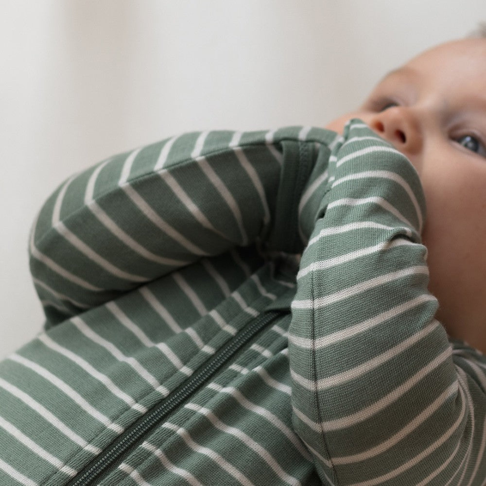 Baby wearing a green and white striped merino outfit against a plain background
