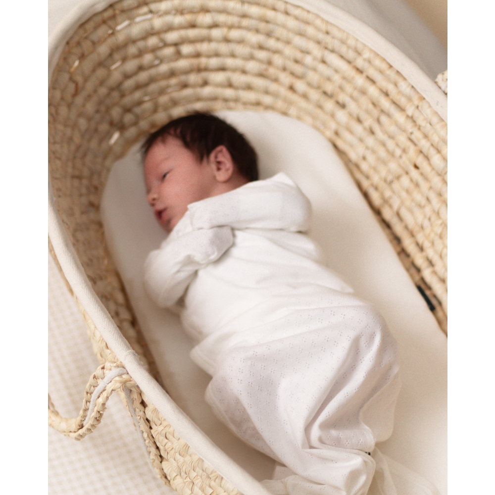 Newborn baby wrapped in white swaddling cloth lying in a woven moses basket.
