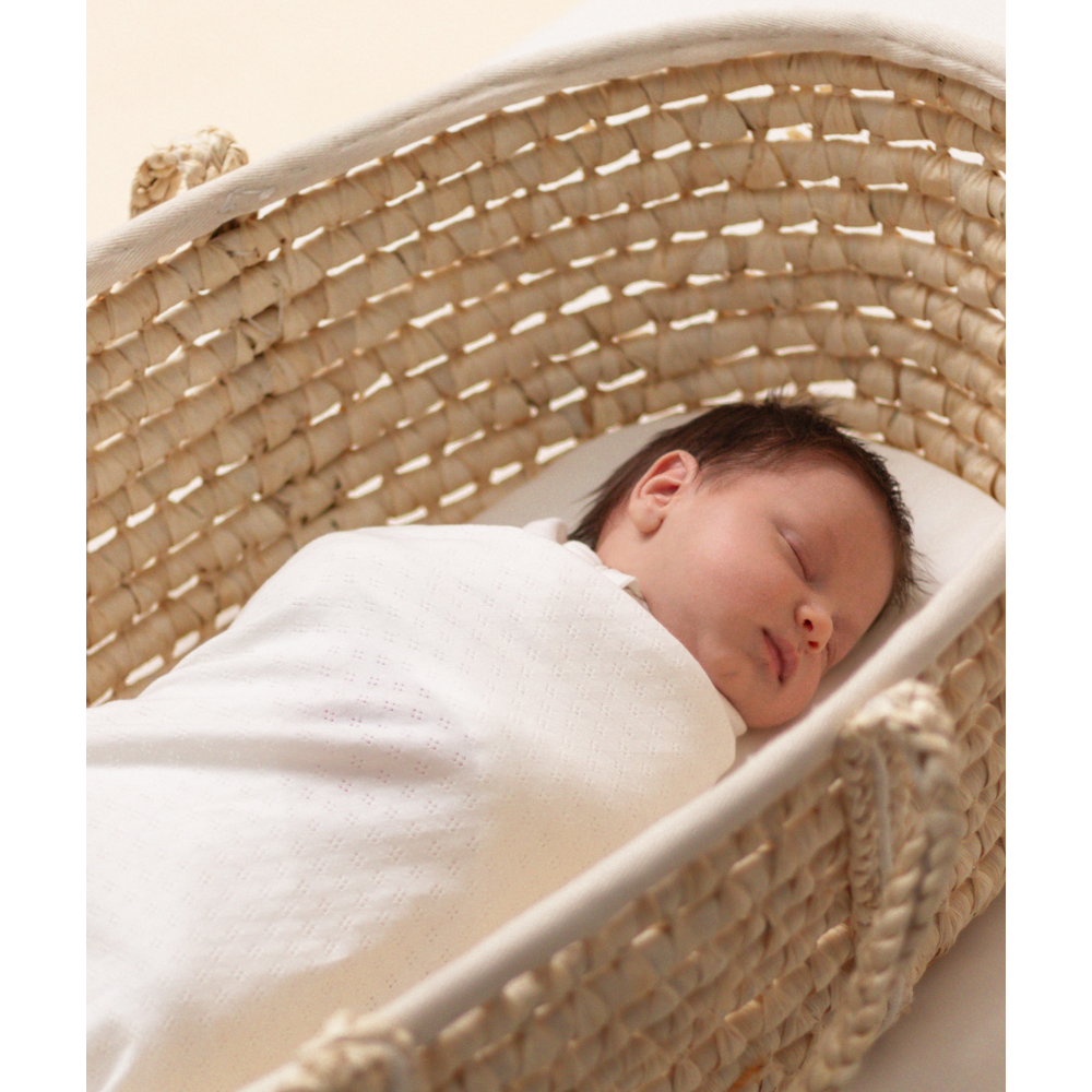 Newborn baby sleeping in a woven moses basket with a white blanket