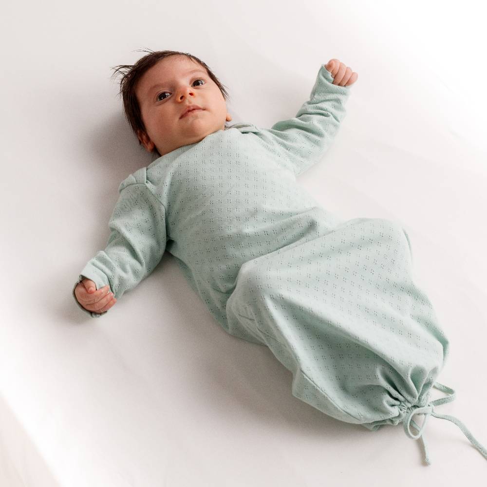 Baby wearing a light green cotton pointelle baby gown on a white background