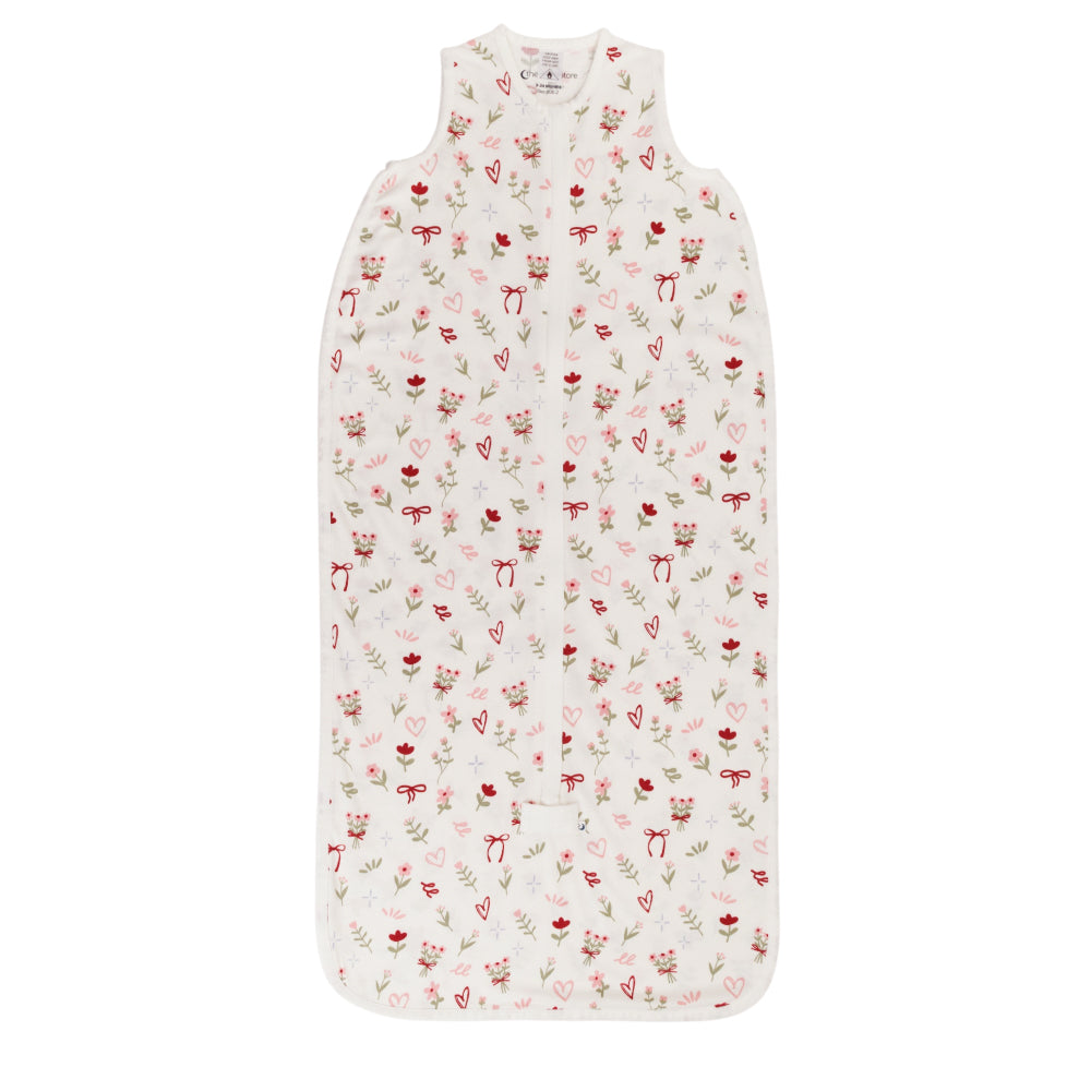 A cotton baby sleeping bag with an all over bows, flowers and hearts print on a white background. 