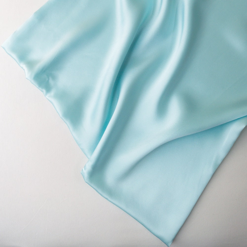 Light blue silk fabric draped elegantly on a plain white surface, showing its smooth, glossy texture.