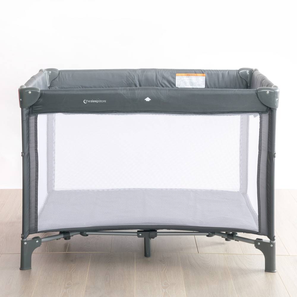 Gray baby travel cot on a wooden floor with a white background