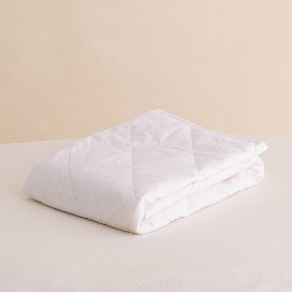 Folded white comforter on a beige bed