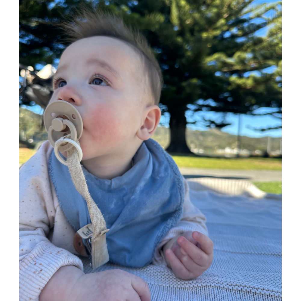 Baby wearing a blue bib and holding a pacifier outdoors