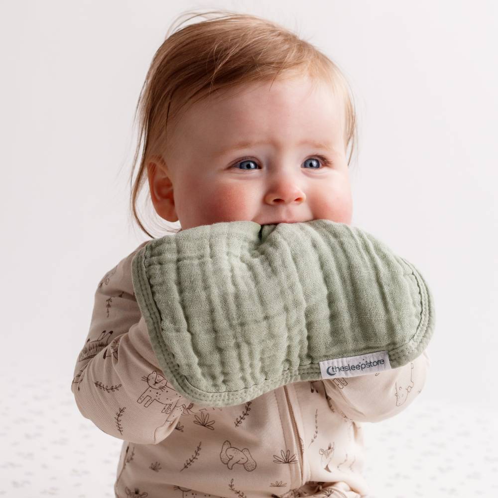 Baby holding a green wash cloth with a visible brand label on a light background