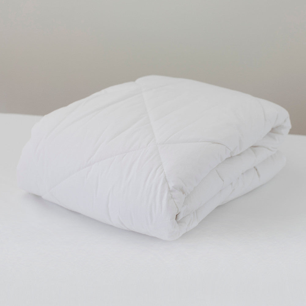Folded white comforter on a bed with a neutral background