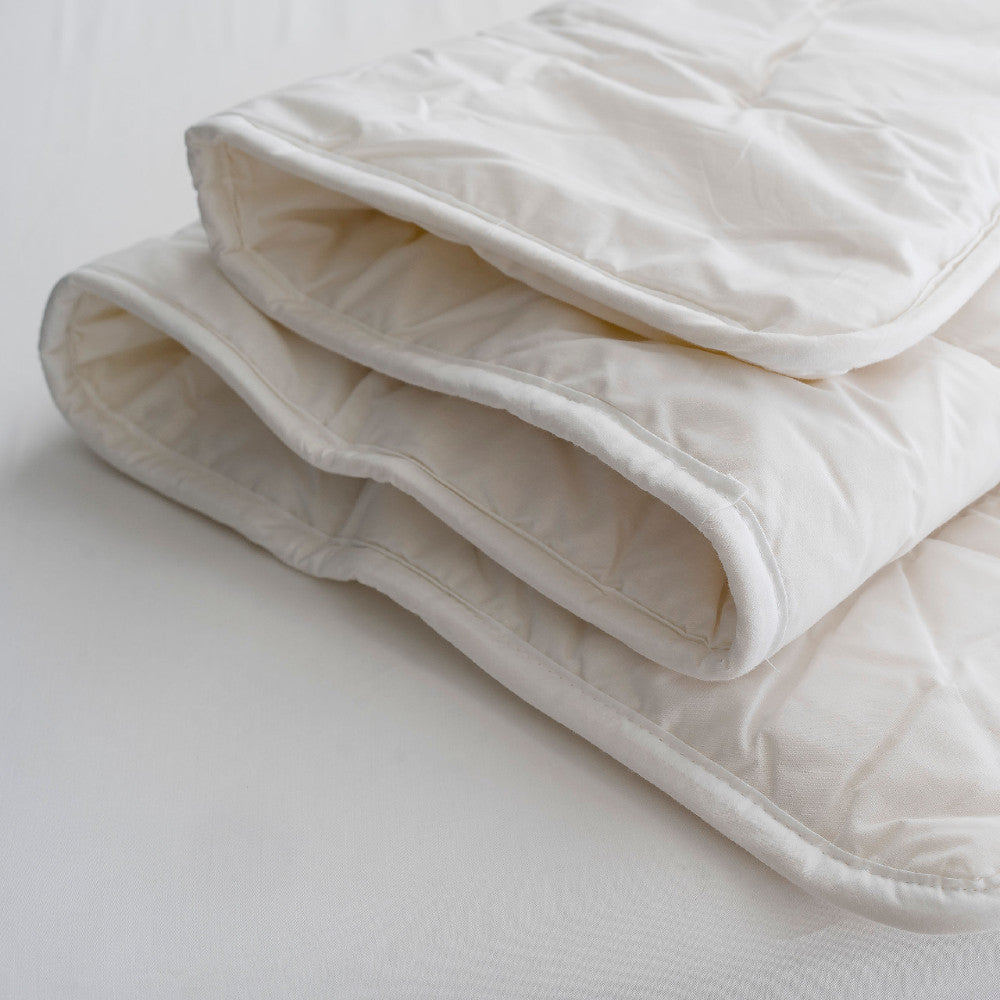 Folded white wool duvet on a light gray background
