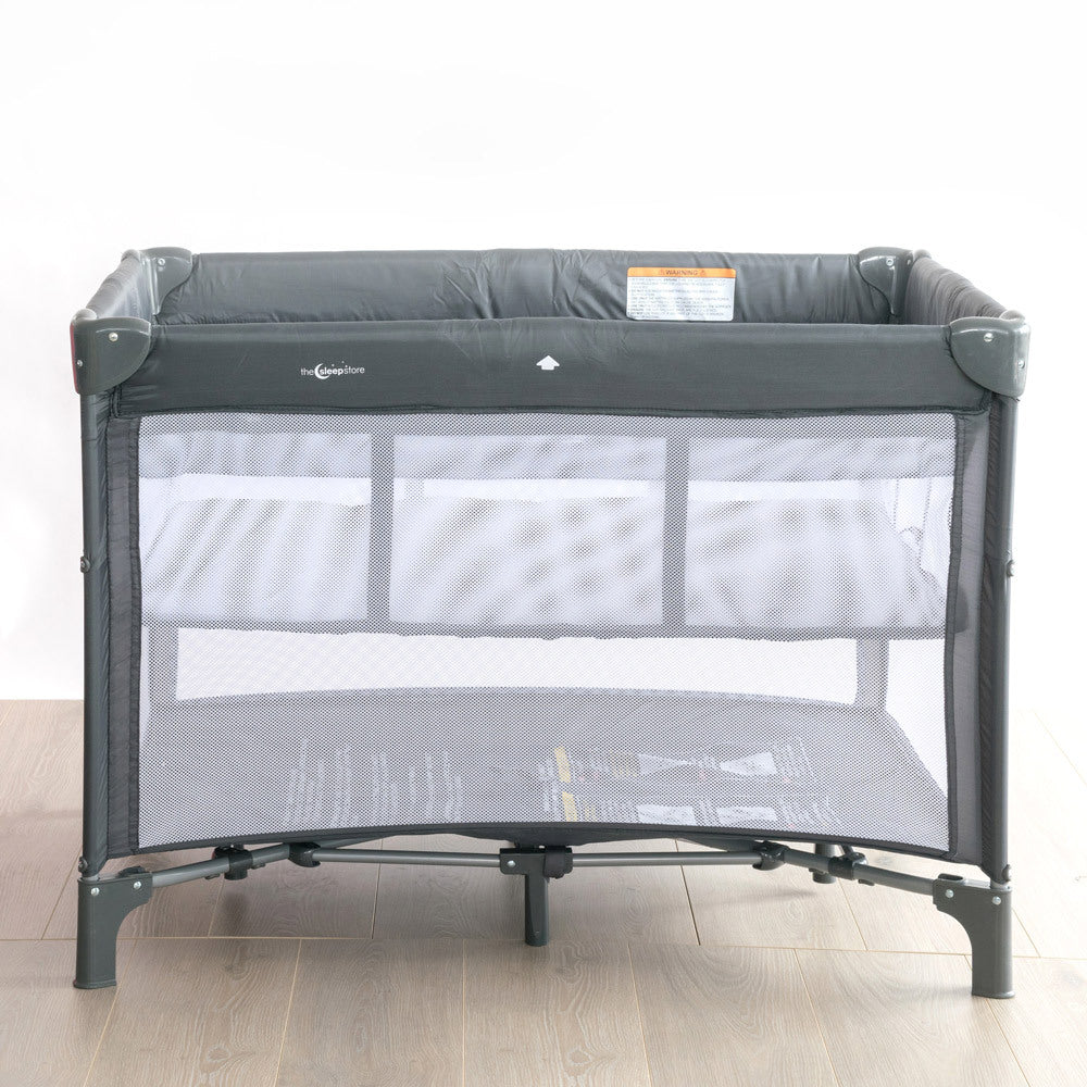 Grey baby portable crib with mesh sides on a wooden floor and white wall