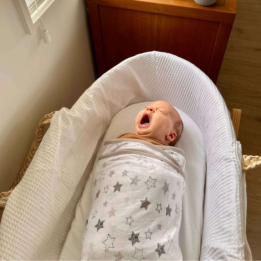 Baby wrapped in a miracle blanket with star patterns in a white moses basket