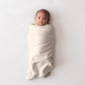 Baby wrapped in a cream coloured miracle blanket swaddle on a white background