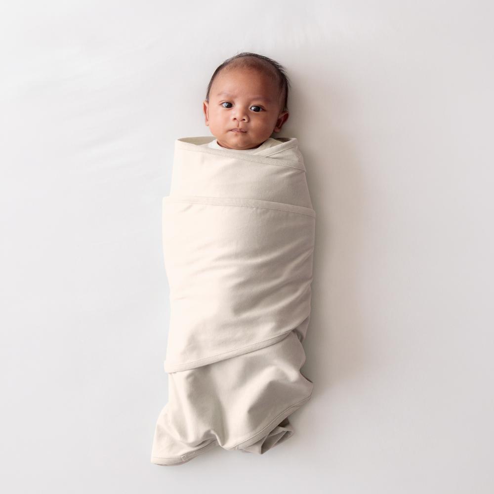 Baby wrapped in a cream coloured miracle blanket swaddle on a white background