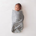 Newborn baby wrapped in a grey miracle blanket swaddle on a white background
