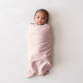 Newborn baby wrapped in a light pink miracle blanket swaddle on a white background
