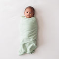 Baby wrapped in a light green miracle blanket swaddle on a white background