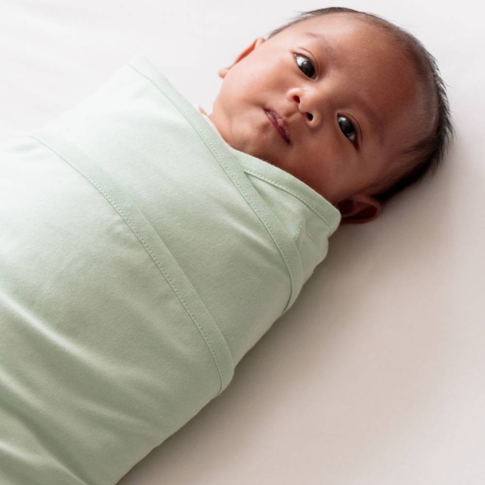 Newborn baby swaddled in a light green blanket on a white background