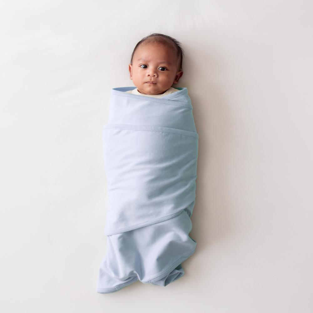 Baby swaddled in a light blue miracle blanket swaddle on a white background