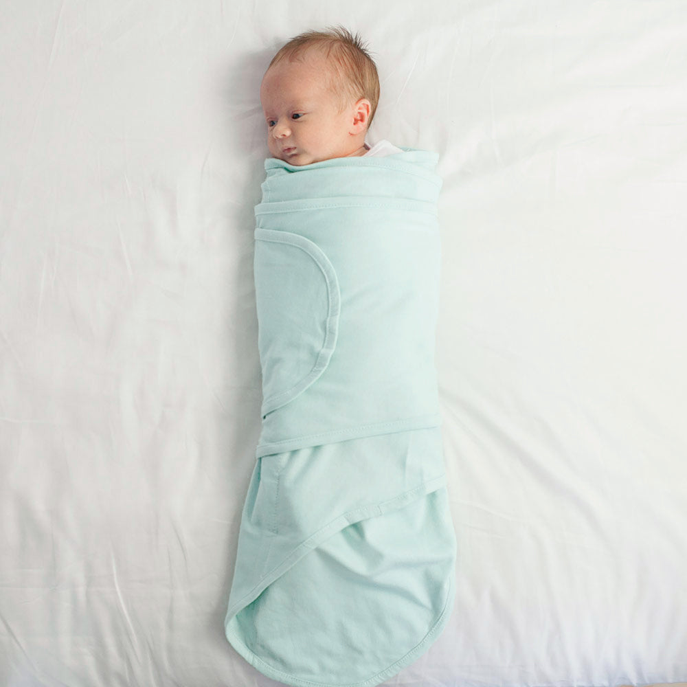 Baby wrapped in a mint coloured miracle blanket swaddle on a white background