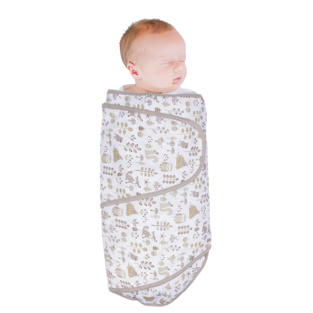 Newborn baby wrapped in a white forest patterned miracle blanket swaddle on a white background
