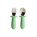 Set of stainless steel baby cutlery with green-handled fork and spoon on a white background