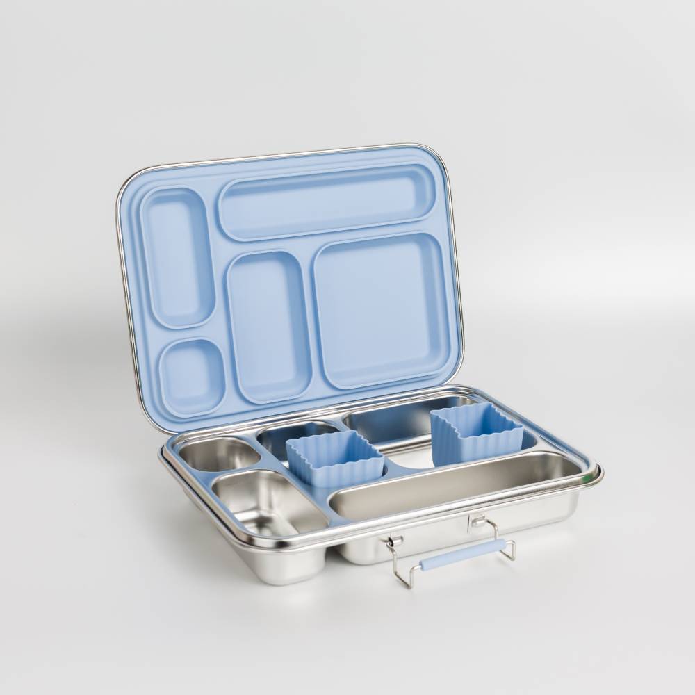 An open stainless steel lunch box with a light blue compartment lid and matching blue silicone insert pieces, photographed on a clean light gray studio background.