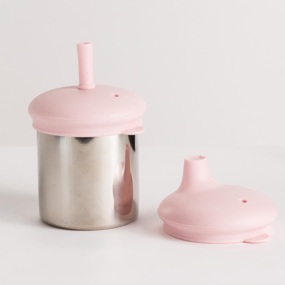 Nestling stainless steel cup with lid with and straw and another pink sippy cup lid on a white background