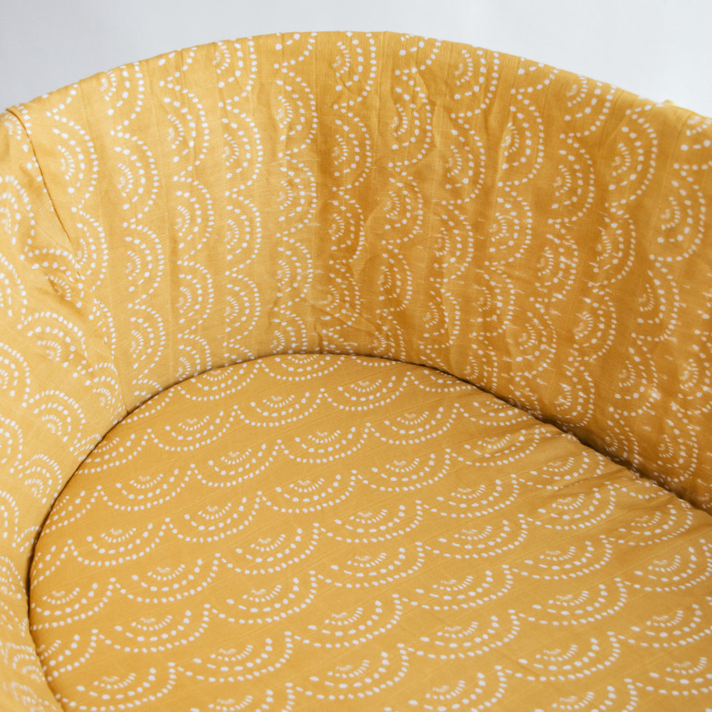 Yellow sunshine print fitted sheet on a mattress inside a moses basket. 