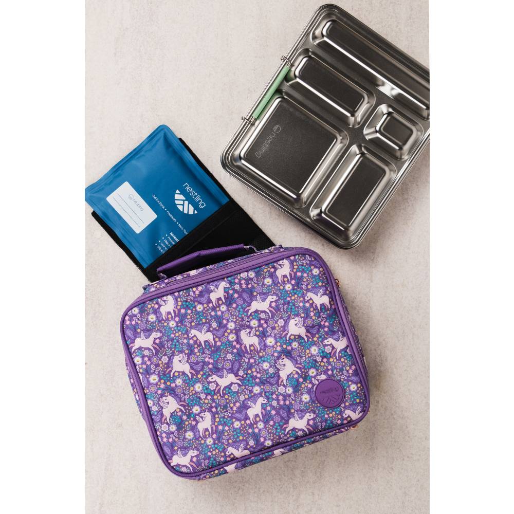 A purple patterned lunch bag with unicorn prints is shown on a light beige surface, alongside a blue ice pack and a stainless steel bento box.